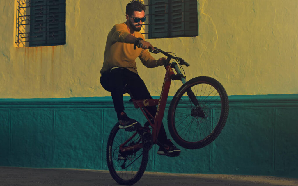 A photo of a man popping a wheelie on a mountain bike in an urban environment.